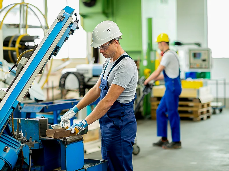 Der Mann im Vordergrund arbeitet an einer Maschine und der Mann im Hintergrund zieht einen Hubwagen.