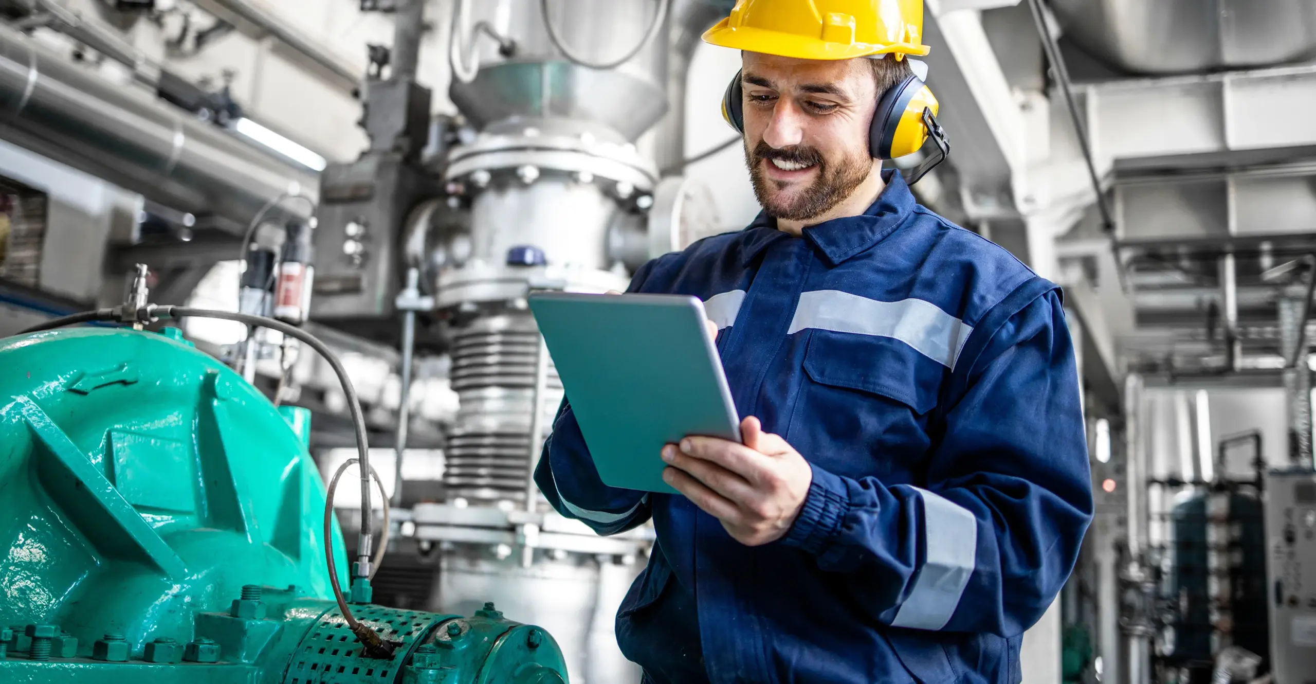 A man in work clothes and a hard hat conducts a risk assessment on a tablet.